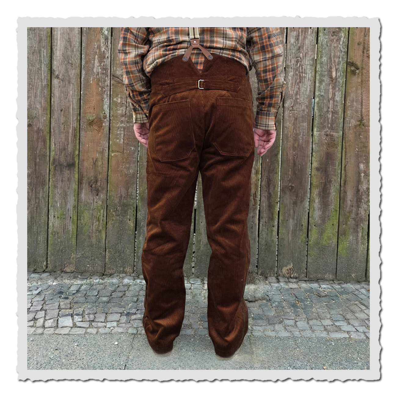 Rückansicht der braunen Cord-Arbeiterhose mit Cinch-Back, großen Gesäßtaschen und geradem Bein, inspiriert von klassischer Workwear vor Holzwand.